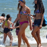 Hot beach brunette in shorts and bikini top with her friend in bikini Hot beach brunette and her friend
